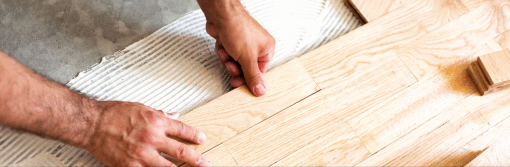 Man installing hardwood flooring over concrete.